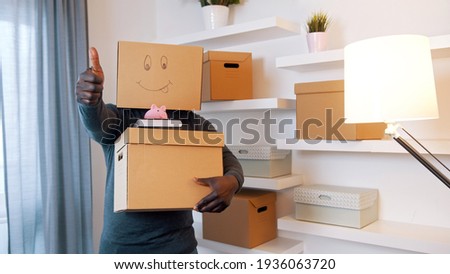 Thumbs up. Unrecognizable man with carboard box over the head package books and piggy bank relocating in new property. Investing in real estate concept. High quality photo