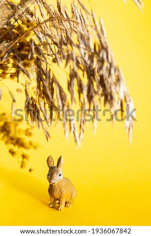 Easter bunny and dried flowers on a yellow background. Modern easter concept, copy space, selective focus. Minimal creative postcard layout.