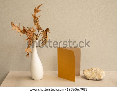Mock up invitation brown cards and exotic Philodendron dry leaves in modern vase on marble table with concrete background,greeting card in earth tone still life