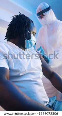 Vertical. Nurse in protective suit giving vaccine against coronavirus to african american black man. High quality photo