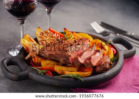 Dinner. Steak with baked vegetables on dark wood board,  and red wine glases.