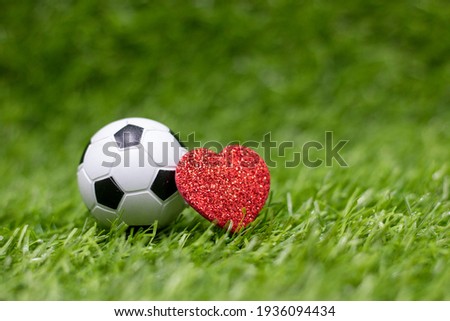 Soccer ball with red heart is on green grass
