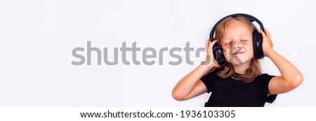 A narrow photo of a small beautiful girl in large headphones and with her eyes closed.