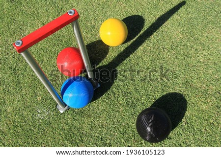 Looking down onto a set of red, blue, black and yellow croquet balls and a croquet hoop with a red cross bar on a green croquet lawn on a sunny day Royalty-Free Stock Photo #1936105123