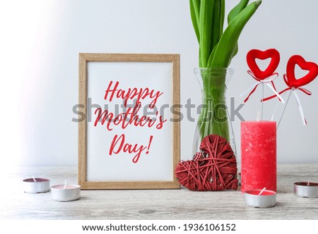 Text Happy Mothers day greeting card. Holiday mock up. Tulip flowers in glass vase with picture frame decor on wooden table background wall at home, close up, design concept.