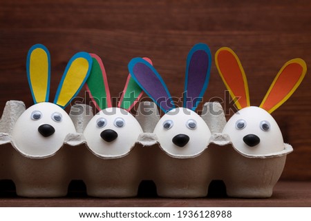 Easter concept (do it yourself):  four   eggs with bunny's eyes, nose and ears in egg container.