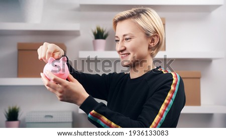 Portrait of young happy caucasian woman putting coins into the piggy bank. High quality photo