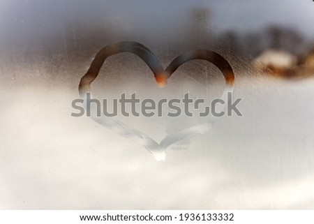 The heart is drawn with a finger on the natural background of the fogged glass in close-up. The image of love