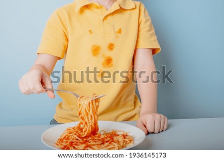 A child's hand holds spaghetti a fork with spaghetti over a plate. concept of dirty stains on clothes. isolated on blue background. High quality photo Royalty-Free Stock Photo #1936145173