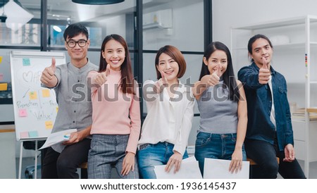 Group of Asia young creative people in smart casual wear smiling and thumbs up in creative office workplace. Diverse Asian male and female stand together at startup. Coworker teamwork concept. Royalty-Free Stock Photo #1936145437