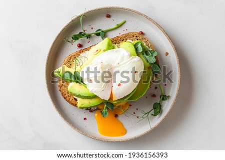 Whole wheat toasted bread with avocado, poached egg, pea sprouts and cheese over white background. Top view. Healthy diet breakfast Royalty-Free Stock Photo #1936156393