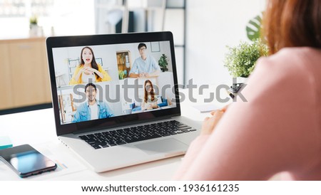 Young Asia businesswoman using laptop talk to colleague about plan in video call meeting while work from home at living room. Self-isolation, social distancing, quarantine for corona virus prevention. Royalty-Free Stock Photo #1936161235