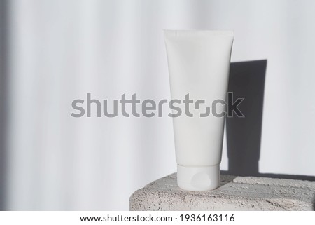 white cosmetic tube for face or body cream, cleanser or shampoo on a concrete podium against a wall background with geometric shadows. Concept of minimalism in cosmetic packaging. Copy space Royalty-Free Stock Photo #1936163116