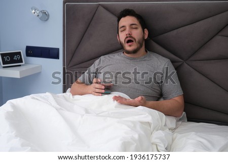 Young latin man ill in bed feeling pain, taking a pill and a glass of water. Feeling sick concept. Royalty-Free Stock Photo #1936175737