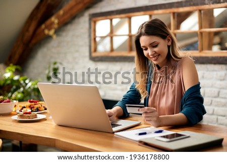 Young happy woman using credit card and laptop while shopping on the internet at home. Royalty-Free Stock Photo #1936178800