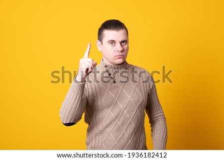 Young handsome man wearing casual sweater over yellow background pointing with finger up and angry expression, showing no gesture.