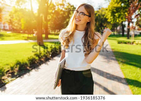 Excited young business woman with laptop, rejoicing at her success and victory, clenching her fists for joy, outdoors on a summer day