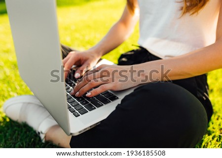 Female hands working on modern laptop, outdoors on a green lawn in the park