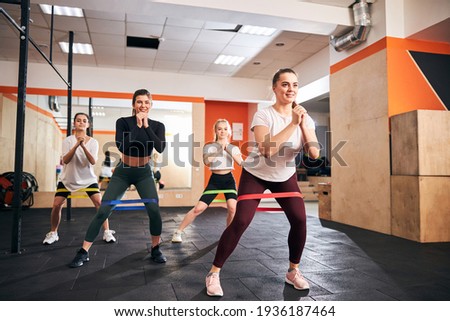 Excited young female athletes keeping themselves in shape by regular exercising with resistance bands Royalty-Free Stock Photo #1936187464