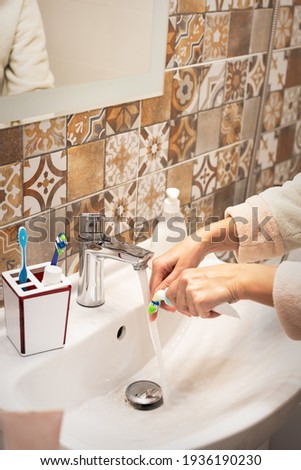 Personal oral hygiene. A young woman squeezes the paste onto her toothbrush. Toothbrush, toothpaste, bathroom accessories. An impersonal portrait of a woman. Hands close-up. Bathroom interior.