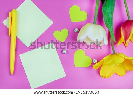 Yellow sheets of paper for writing (notes), colorful tulips, a pen and hearts on a bright pink background. Space for the text. The concept of love and celebration. Valentine's Day, March 8, birthday.