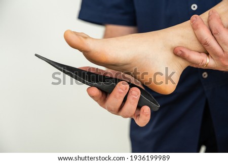 Doctor specializing in plantar posturology in his medical office tests the orthopedic device insoles on the patient's foot - Flatfoot treatment in podiatry clinic Royalty-Free Stock Photo #1936199989