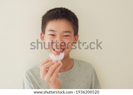 Smiling Asian preteen boy holding invisalign braces, mouthguard, teen orthodontic oral health care concept Royalty-Free Stock Photo #1936200520