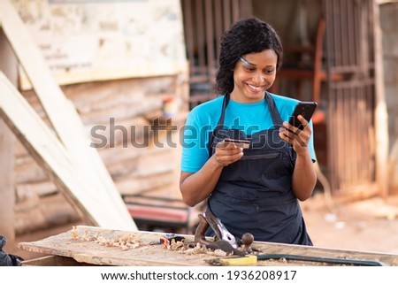 female african carpenter using her phone and credit card, paying online