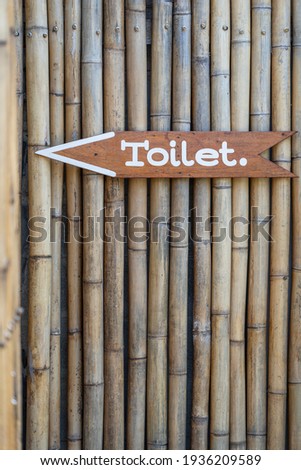 Text toilet on wooden board on bamboo wall on tropical island Koh Phangan, Thailand. Vertical view of simple design handmade wooden sign of toilet give direction to WC . Close up, outdoors