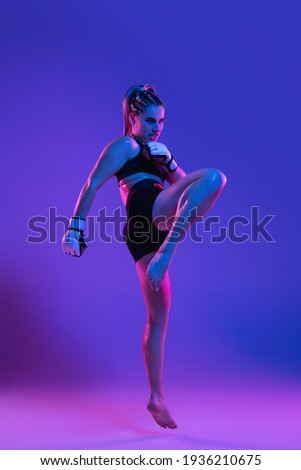 Knee kick. Young woman strong athletic female MMA fighter training isolated on gradient blue-pink background in neon light. Concept of sport, competition, action, healthy lifestyle. Copy space for ad. Royalty-Free Stock Photo #1936210675