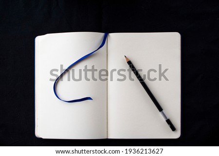 Open blank notebook with a pencil on top of the pages, on a black background