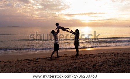 Silhouette picture of father and mother playing with toddler son with happiness moment on the beach in the background of sunrise in the morning time, concept of vacation time of family lifestyle.