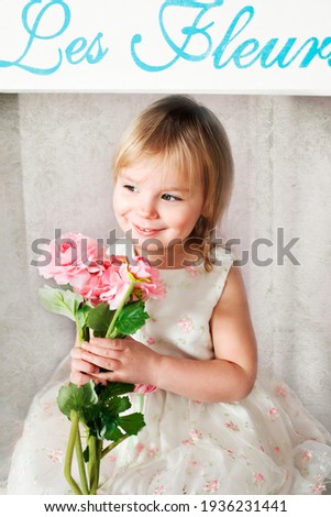 Beautiful blonde girl with bouquet of pink flowers on background of decorated flower shop. Easter, flower business concept. Inscription in French "Flowers"