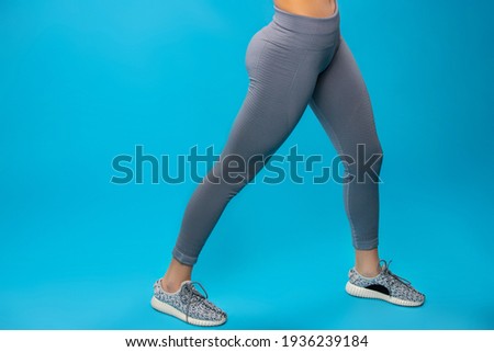 Fashion sportswear. Cropped photo of fit long female legs wearing ultimate grey color of leggings and sporty sneakers on blue background