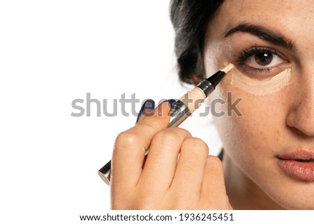 Half portrait of young beautiful woman applying concealer with applicator on white background Royalty-Free Stock Photo #1936245451