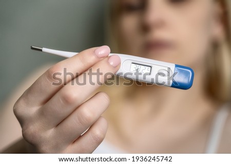 Close-up thermometer. Mother measuring temperature of her ill kid. Sick child with high fever laying in bed and mother holding thermometer. Hand on forehead. Royalty-Free Stock Photo #1936245742