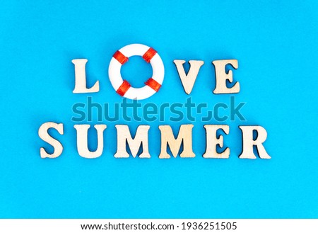 Lettering LOVE SUMMER made of wooden characters and a toy lifebuoy on a blue background.