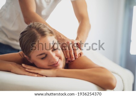 Professional masseur doing therapeutic massage. Woman enjoying massage in her home. Young woman getting relaxing body massage. Royalty-Free Stock Photo #1936254370