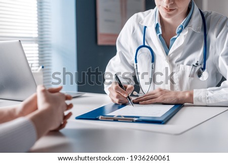 Doctor sitting at desk and writing a prescription for her patient Royalty-Free Stock Photo #1936260061