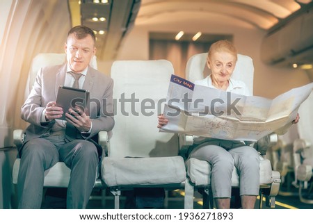 The passengers this flight oneman wacting the stock exchange on his ipad check for his business company and old woman read map paper of destination city