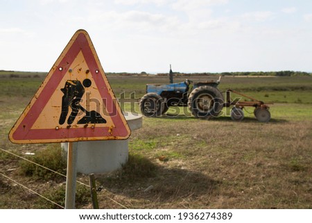 warning sign for work in progress on public roads and in the field parked old but working tractor with plow trailer