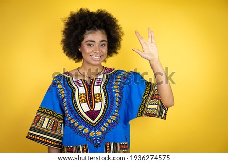 African american woman wearing african clothing over yellow background doing hand symbol