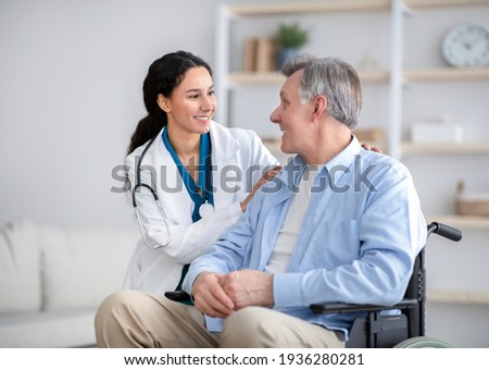 Impaired senior man in wheelchair and young nurse taking care of him at home Royalty-Free Stock Photo #1936280281