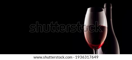 A glass and a bottle of red wine on a black background. panoramic photo, copy space