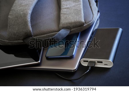 Modern gadgets - a smartphone, tablet and laptop or ultrabook - lie in a gray city backpack next to a large external battery - power bank. Charge your gadgets while traveling and trip. Close-up