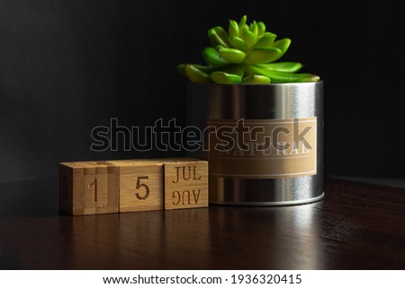 July 15. Image of the calendar July 15 wooden cubes and an artificial plant on a brown wooden table reflection and black background. with empty space for text