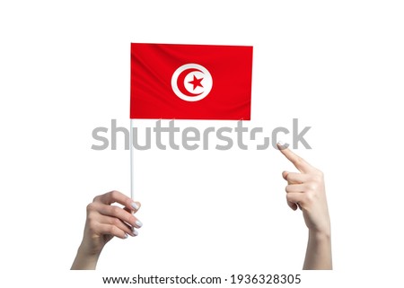 A beautiful female hand holds a Tunisia flag to which she shows the finger of her other hand, isolated on white background.