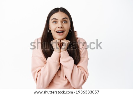 Portrait of excted young brunette girl open mouth wondered, leaning on hands while watching something awesome and beautiful, gasping fascinated, white background Royalty-Free Stock Photo #1936333057