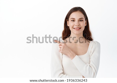 Spring, fashion and lifestyle concept. Confident stylish young woman in outfit, pointing finger left and looking at something with pleased smile, found great product, white background