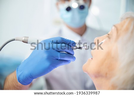 Hand lowering dental handpiece with bur to pensioner teeth Royalty-Free Stock Photo #1936339987